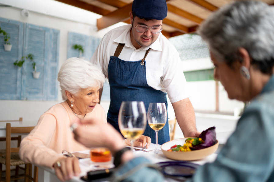 Waiter serving a meal to a table of older women.